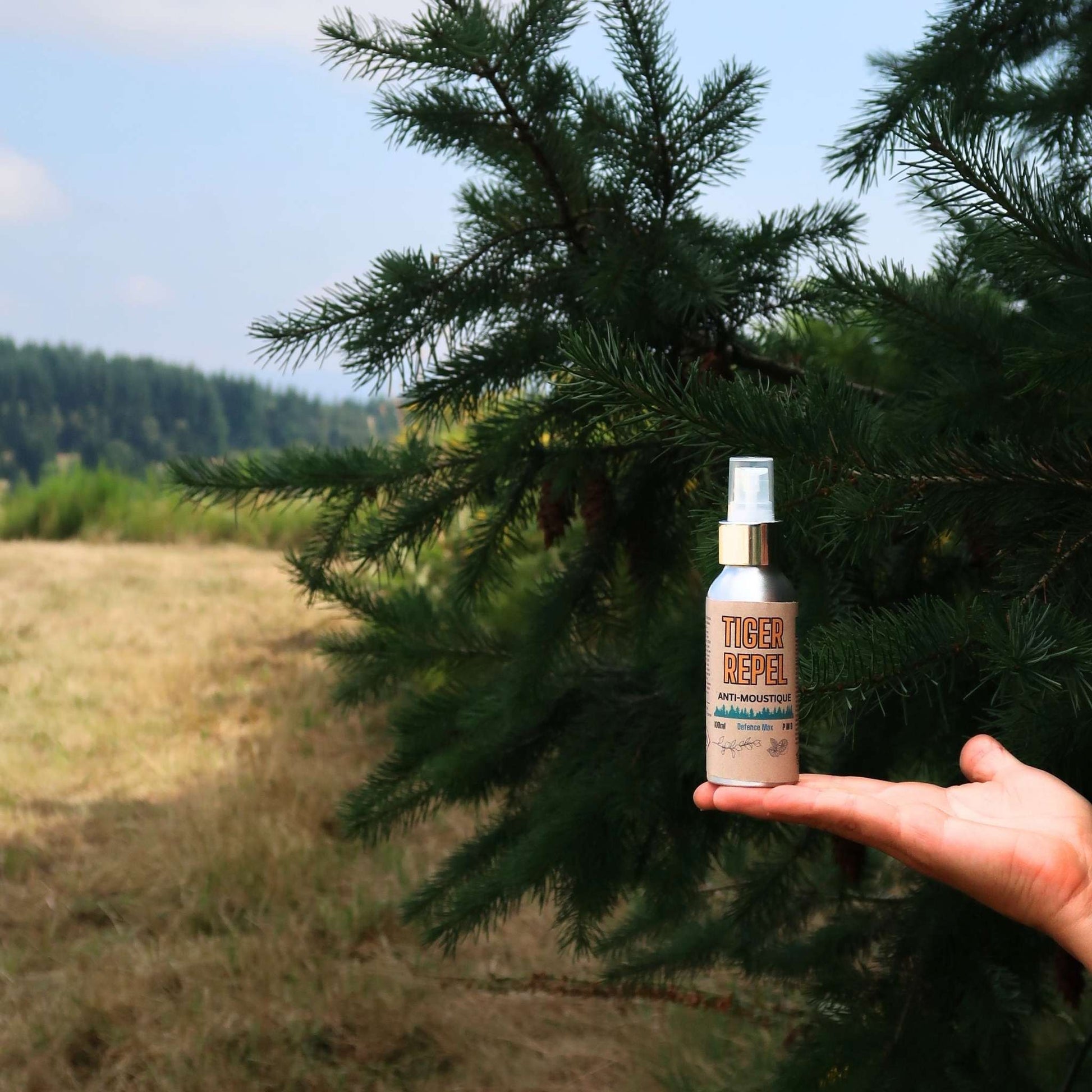 Bouteille de spray anti-moustique naturel Tiger Repel tenue en plein air, devant un paysage boisé, idéal pour repousser les moustiques lors d'activités en extérieur